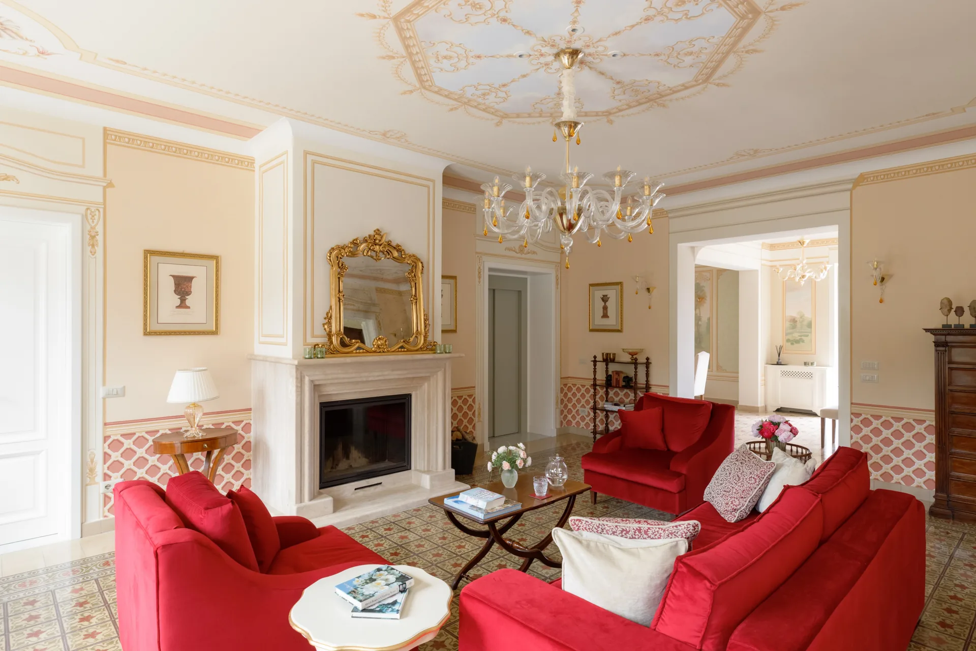 Salón de Villa Marie con sofás rojos, chimenea y espejo dorado