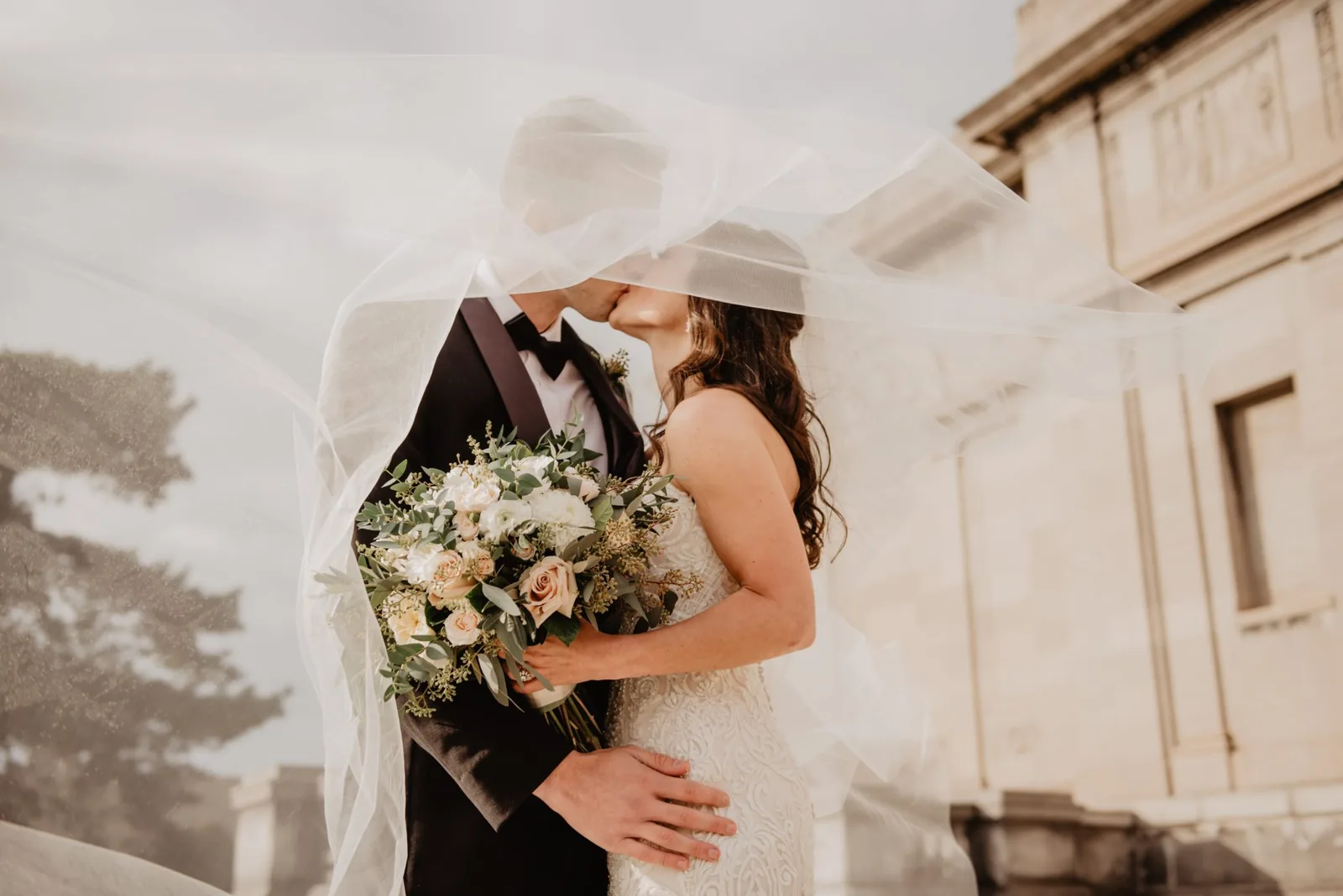 Couple de mariés avec un bouquet sous un voile