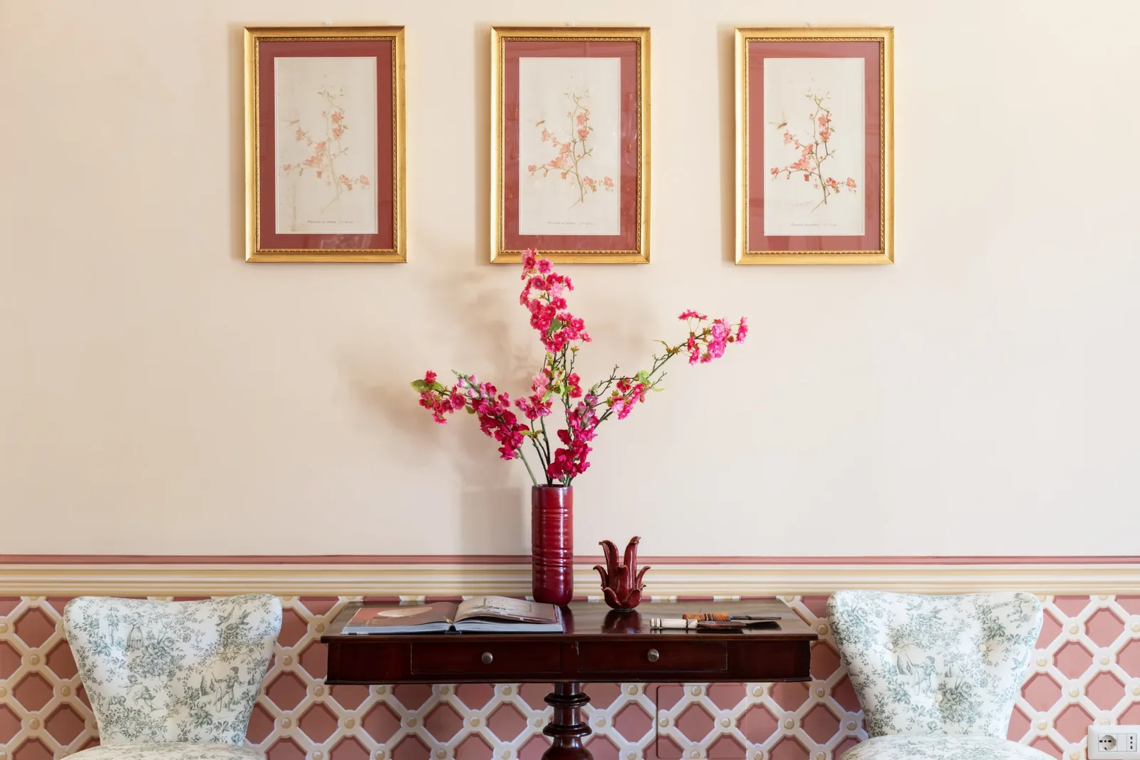 Vase rouge fleuri sous trois gravures dans le salon de Villa Marie